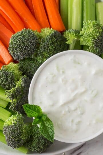 An overhead photo of a bowl of tzatziki with celery, carrots and broccoli.