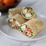 A photo of a sliced curry chicken salad wrap on a white plate.