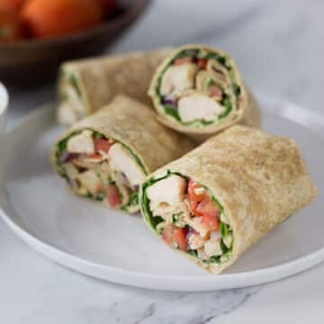 A photo of a sliced curry chicken salad wrap on a white plate.