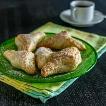 A photo of pastelitos de guava on a green plate with coffee cup in the background.