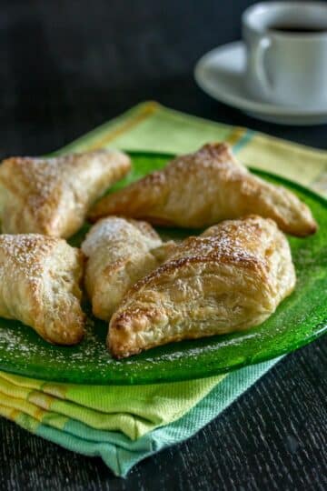 A photo of pastelitos de guava on a green plate with coffee cup in the background.