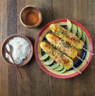 An overhead photo showing three ears of elote or Mexican street corn on a plate.
