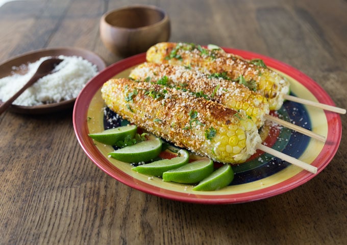 A photo of 3 cooked ears of corn on a plate and seasoned with elote spices.