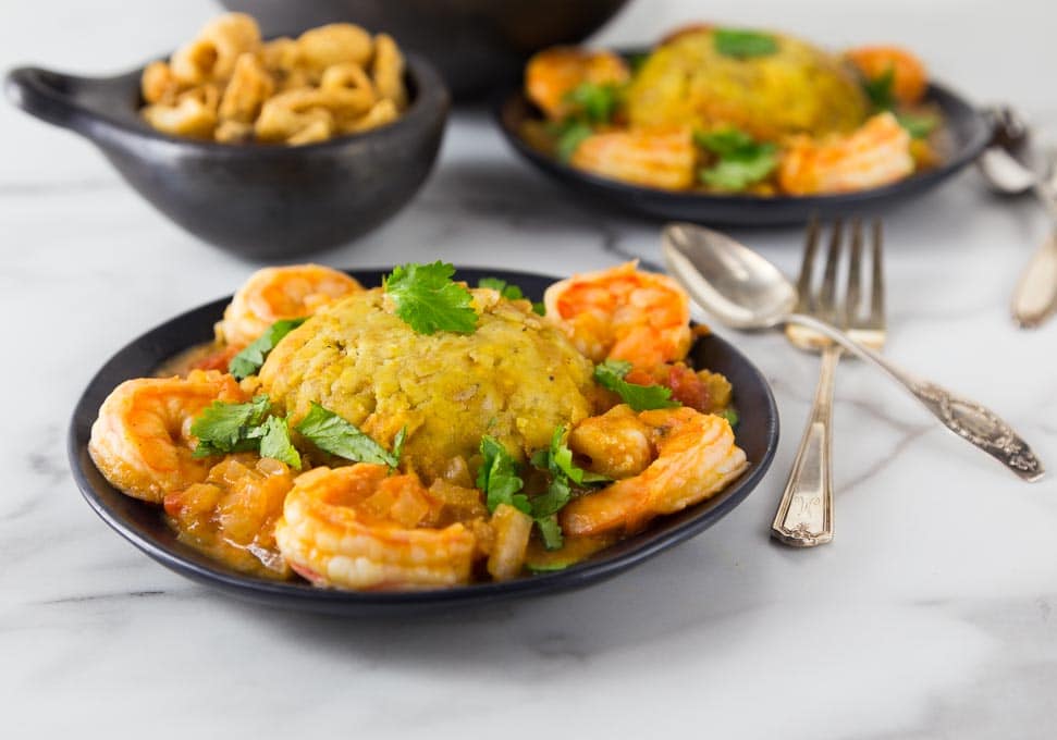 A photo of mofongo on a black plate with shrimp and sauce.