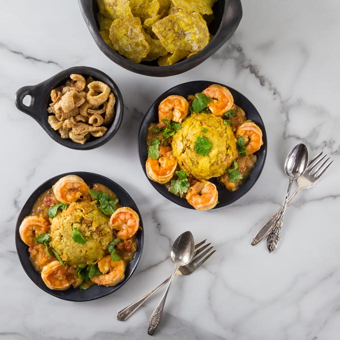 An overhead photo of mofongo on black plates with shrimp and sauce.