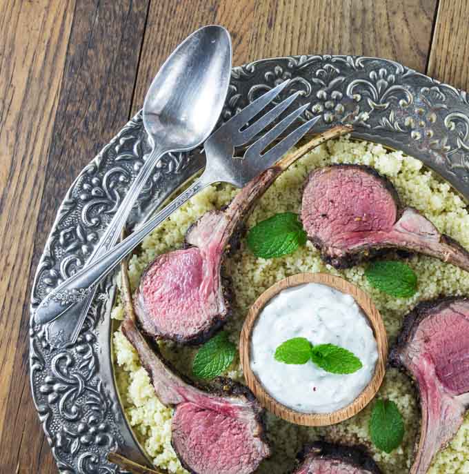 Slice of Turkish rack of lamb on a platter with couscous, mint garlic yogurt sauce and mint leaves.