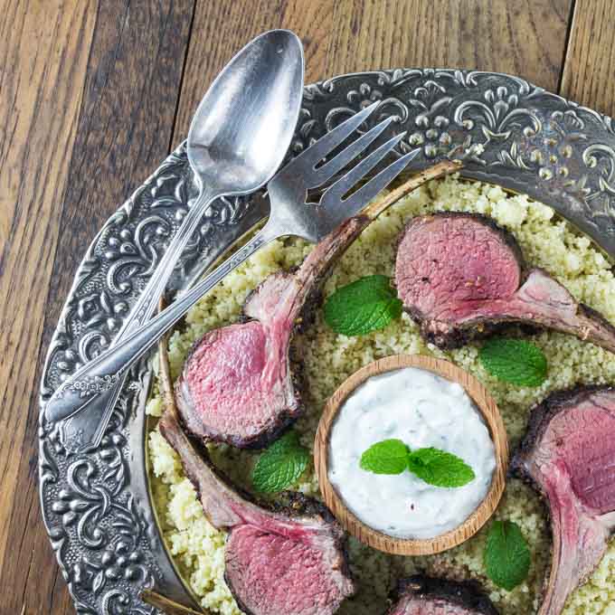 Sliced rack of lamb on a platter with couscous and a fork and spoon.