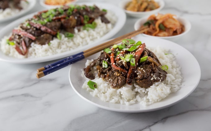 A white plate with rice, beef bulgogi and chop sticks.