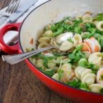 A photo of orecchiette paste with shrimp, fennel and arugula in a red pan with a spoon.