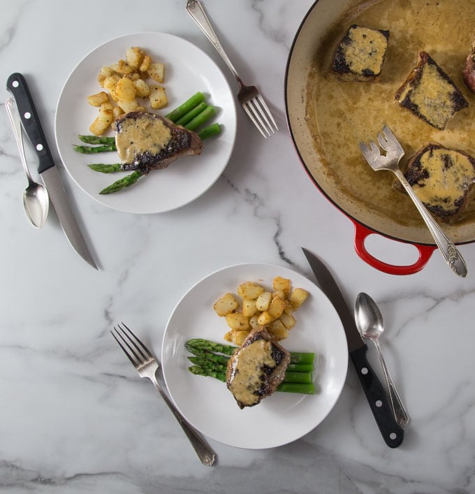 A photos of two white plates with steak au poivre, potatoes and asparagus.