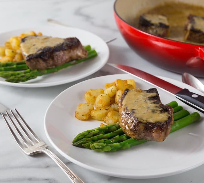 A closeup photo of steak au poivre with asparagus and potato.
