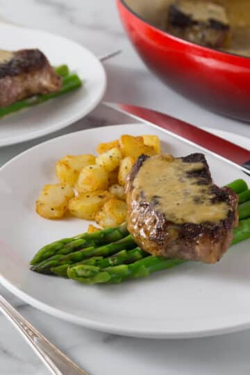 A photo of steak au poivre on a white place with asparagus and potatoes.