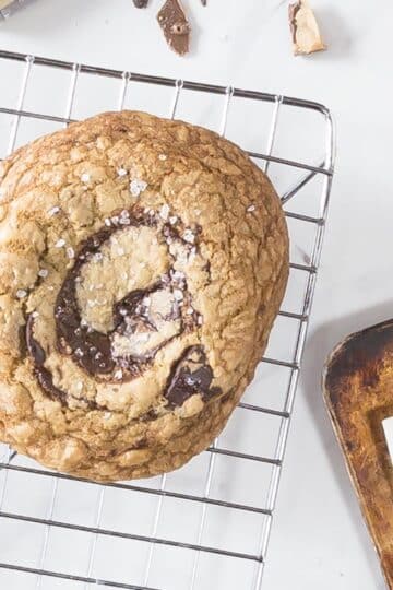 A photo of an English toffee chocolate chip cookie on a cooling rack.