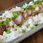 A photo of Thai pork loin slices with rice, peanut sauce and chopped onions.
