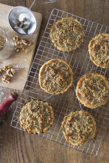 A photo of walnut tartlets on a cooling rack with a rolling pin next to it.