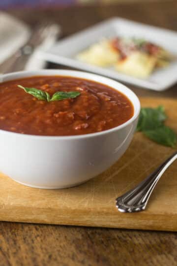 A white bowl with marinara sauce next to a service spoon.