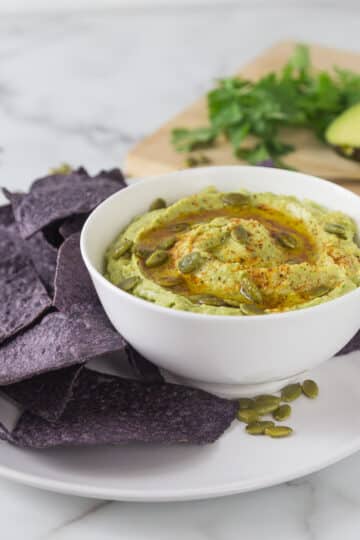 A photo of cannellini bean avocado hummus in a white bowl with blue corn chips.