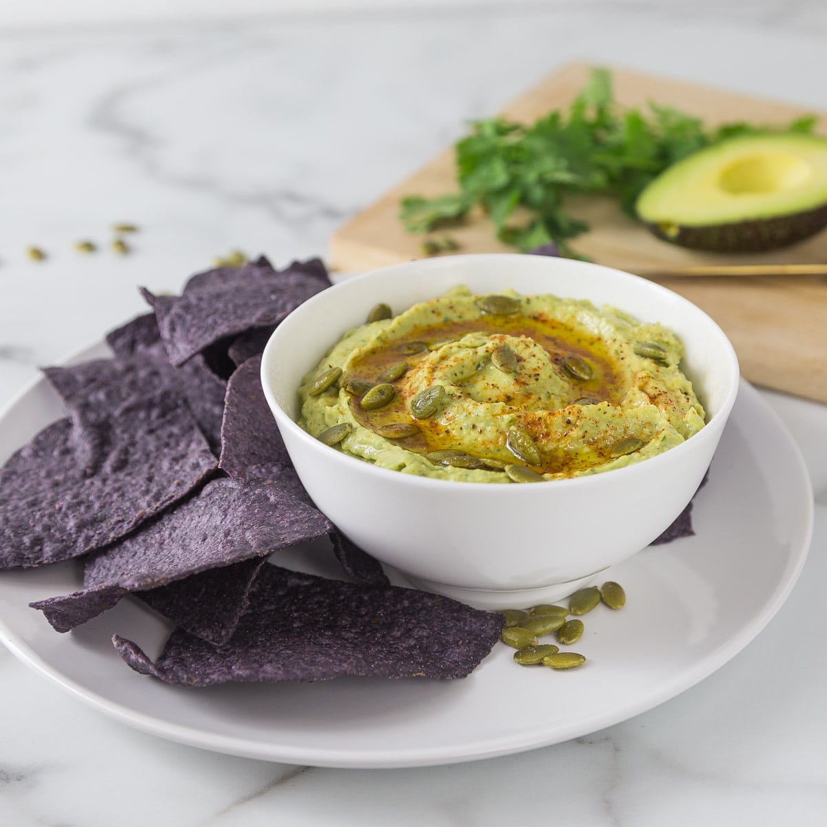 A photo of cannellini bean avocado hummus in a white bowl with blue corn chips.