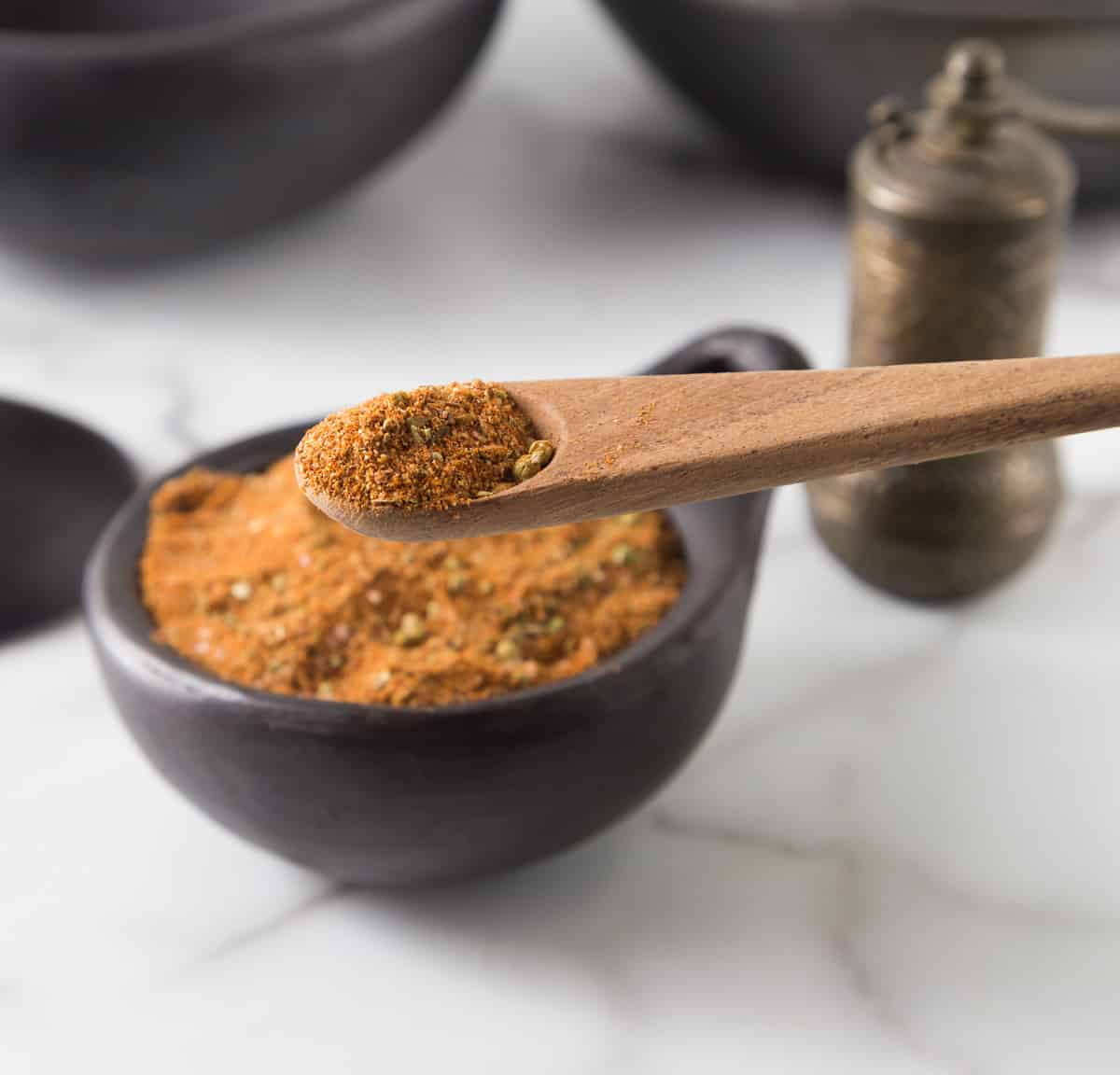 A photo of Turkish seasoning on a wooden spoon with a black bowl in the background.