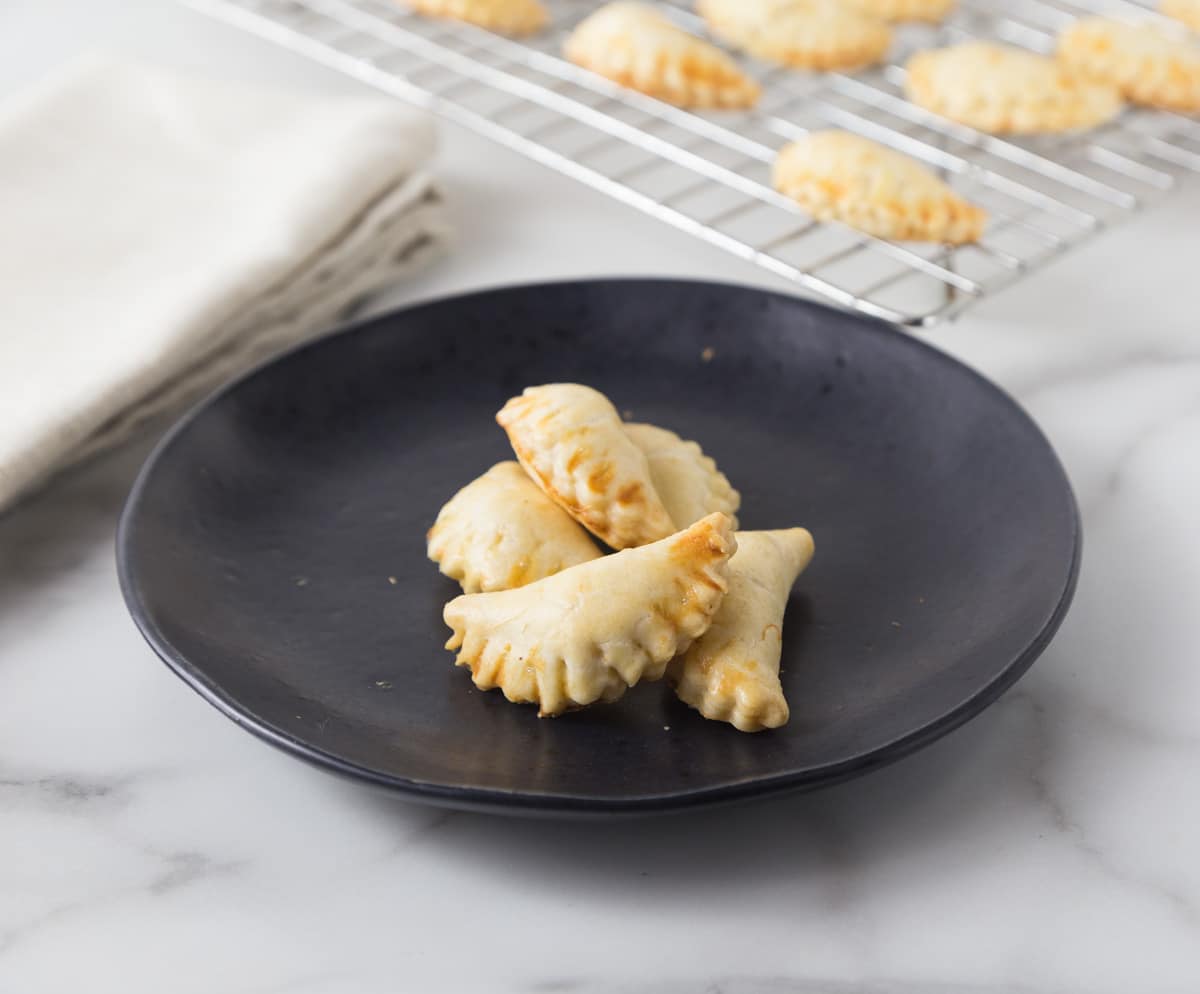 A photo of mini crab meat empanadas in a black plate with a cooling rack in the background.