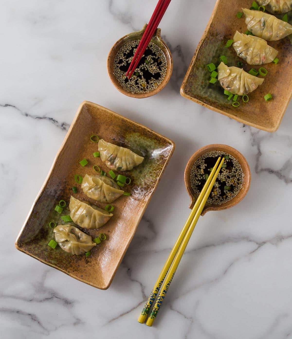 An overhead photo showing brown plates with Thai style chicken pot stickers and small bowl with dipping sauce.