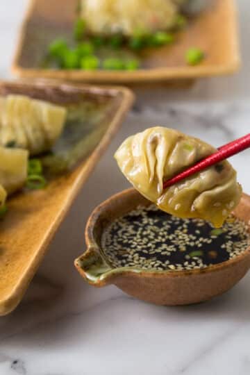 A photo showing red chop sticks holding a Thai style chicken pot sticker.