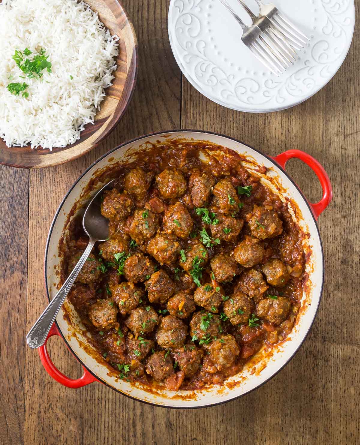 An overhead photo of Persian meatballs or koofteh in saffron tomato sauce with a bowl of rice.