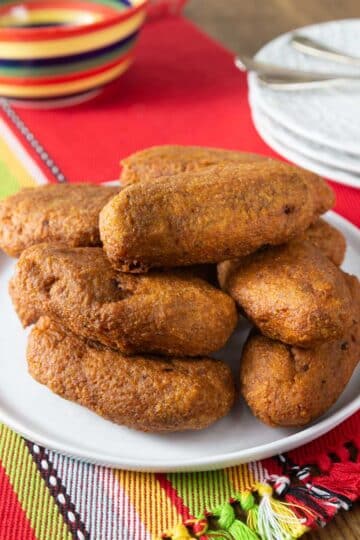 A photo of alcapurrias on a white plate with plates and forks in the background.