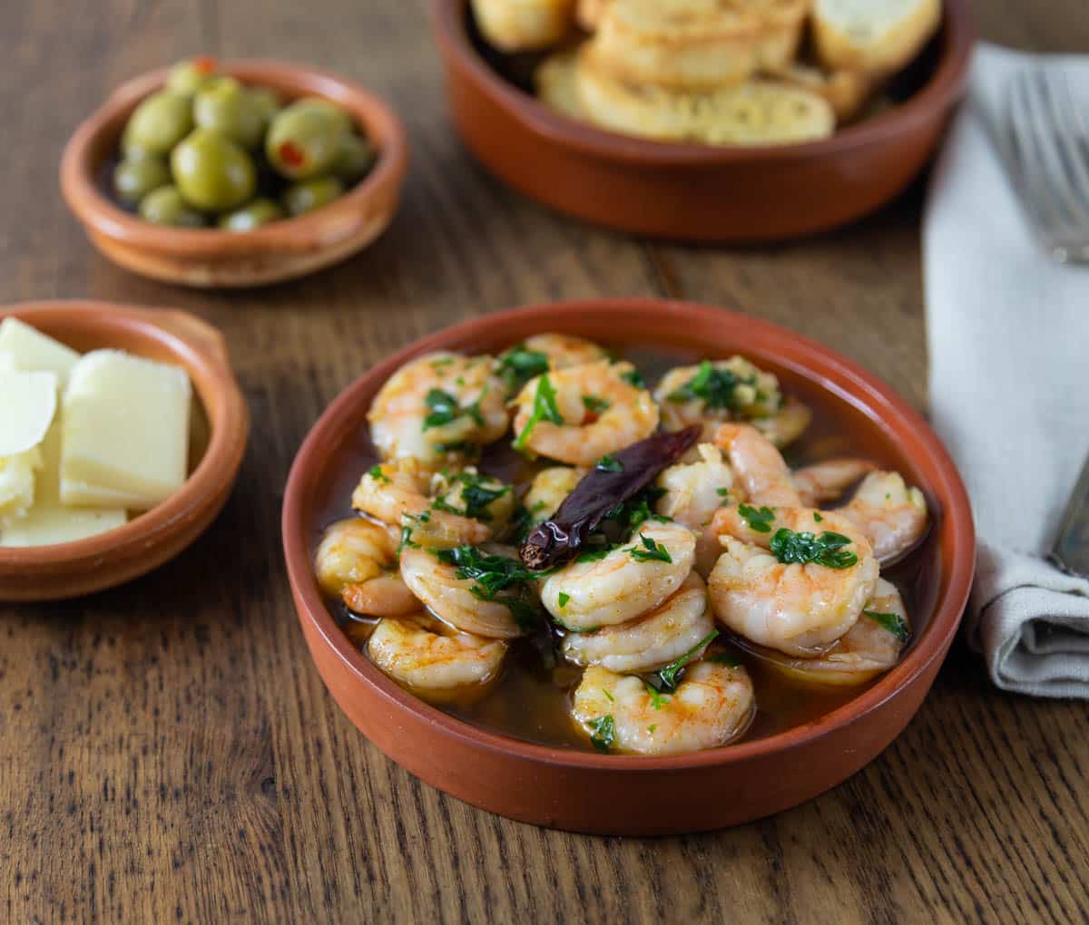 A photo of gambas al ajillio or shrimp in garlic sauce with bread in the background.