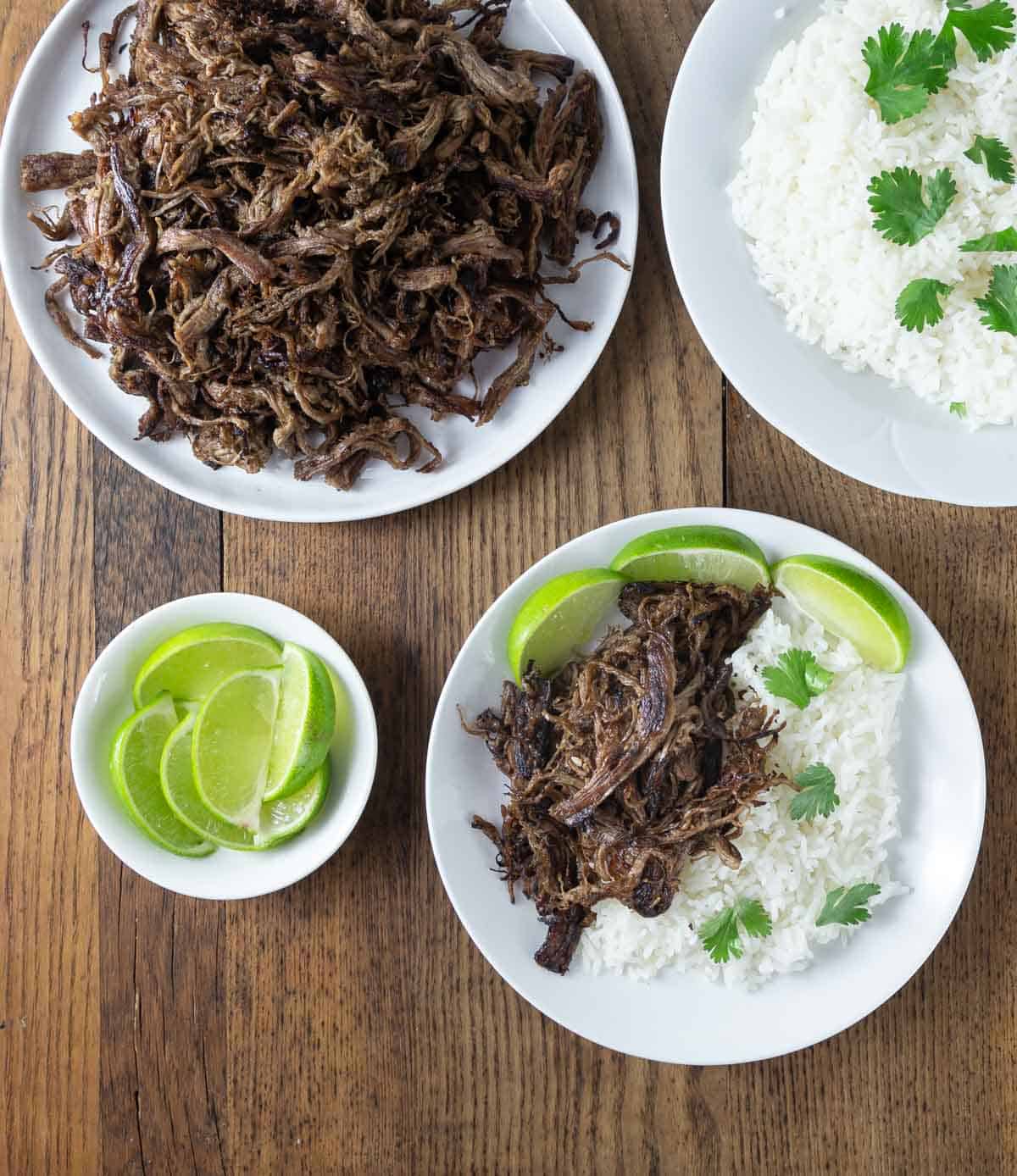 An overhead photo of Cuban vaca frita on a white platter and a plate with rice and slices limes.