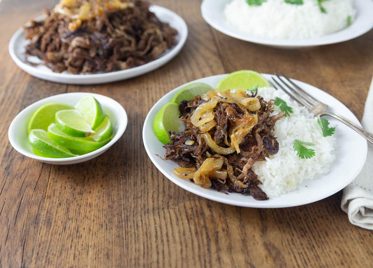 A white plate with Cuban vaca frita along with rice and onions.