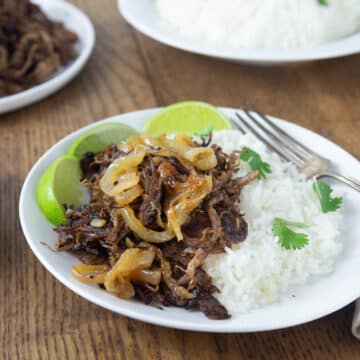 A photo of vaca frita on a white plate with caramelized onions and slices limes.
