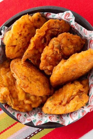 An overhead photo of bacalaitos in a black bowl with a red placemat underneath.