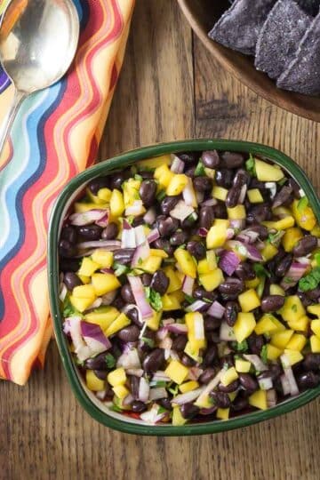 A overhead photo of mango black bean salsa in a bowl with a napkin and spoon.