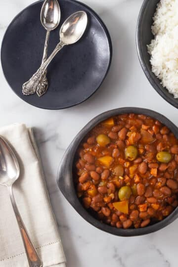An overhead photo of Puerto Rican stewed beans with plates, spoons and a bowl of rice.