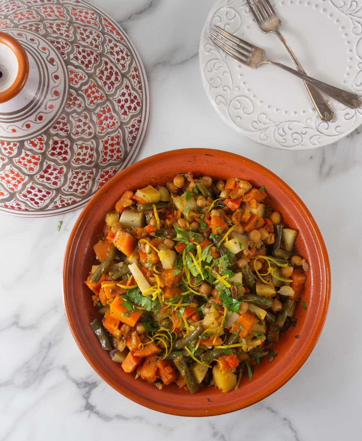 An overhead photo of Moroccan vegetable tagine dish and lid with plates and forks.