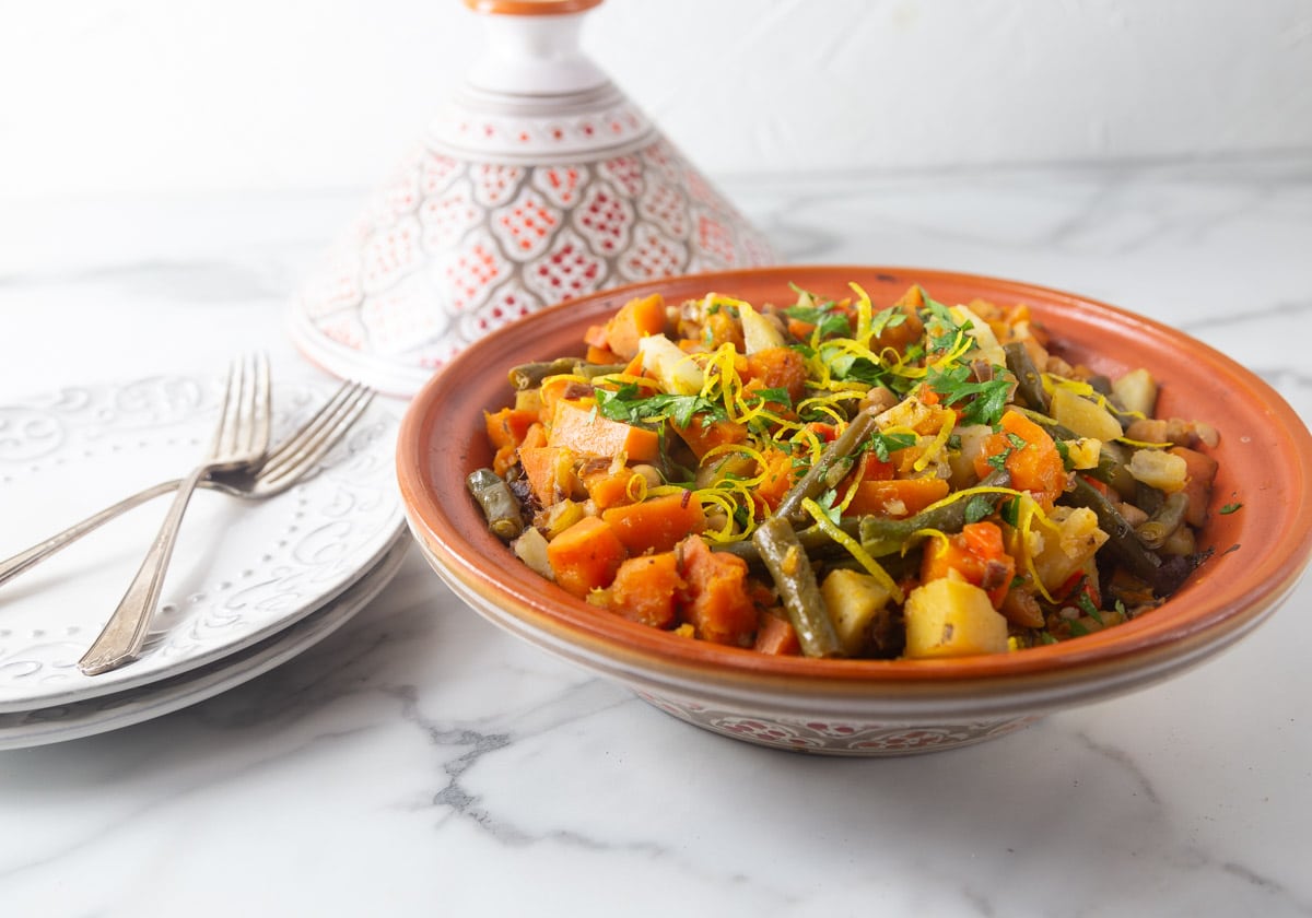 A photo of Moroccan vegetable tagine with the cone lid in the background.