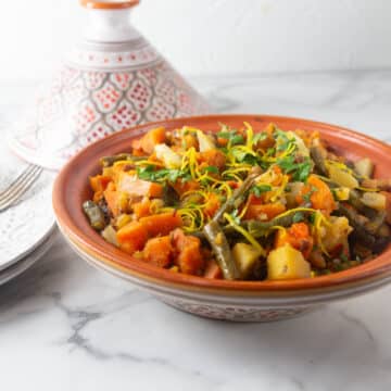 A photo of Moroccan vegetable tagine in on a table with plates in the background.