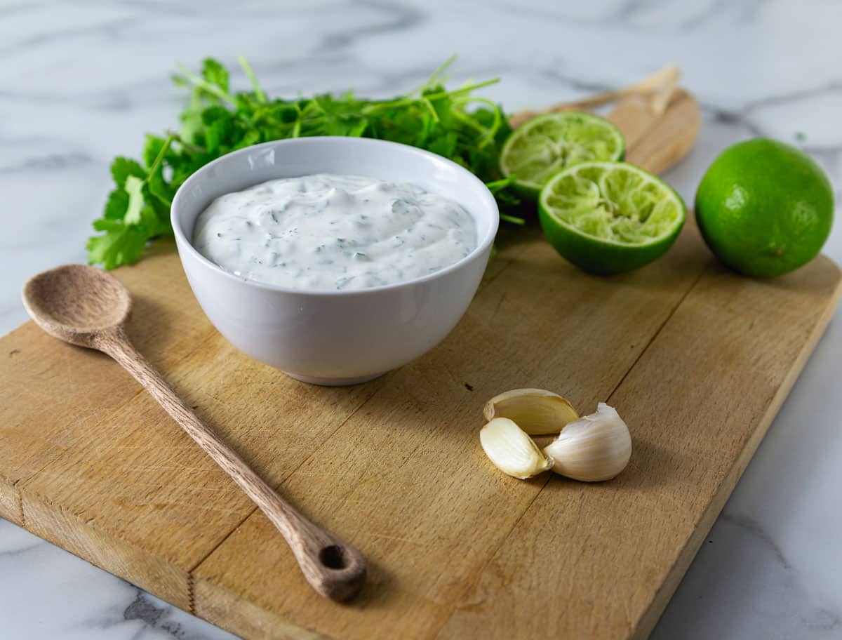 A white bowl with cilantro lime crema and limes in the background.