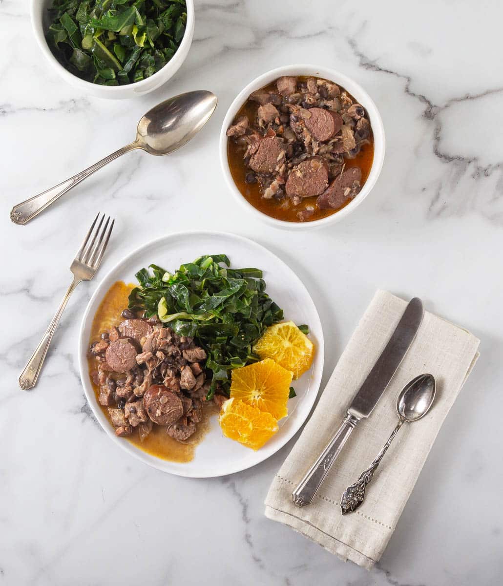 An overhead photo of feijoada on a white plate with silverware.