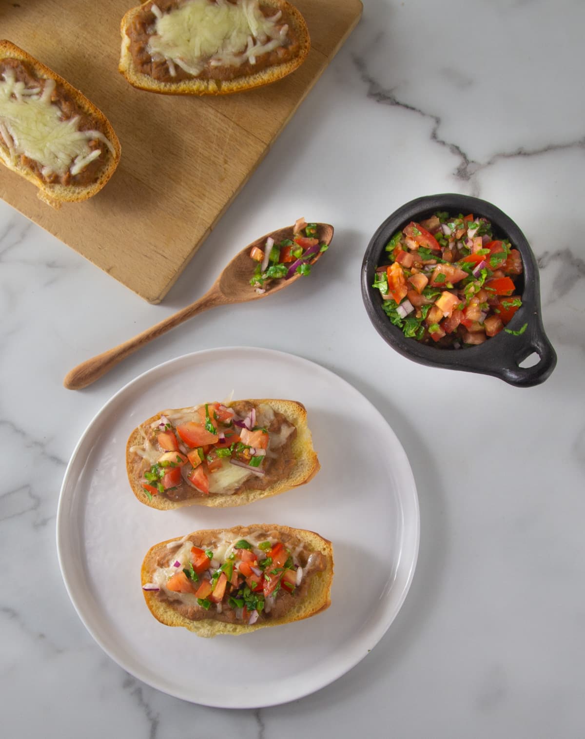 An overhead photo of molletes on a white plate beside a bowl of pico de gallo.