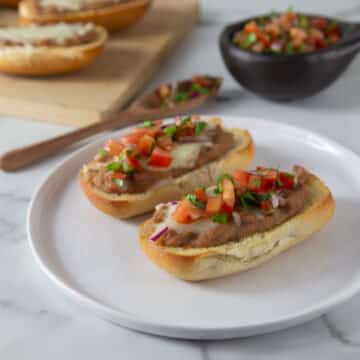 A photo of two molletes on a white plate with pico de gallo on top.