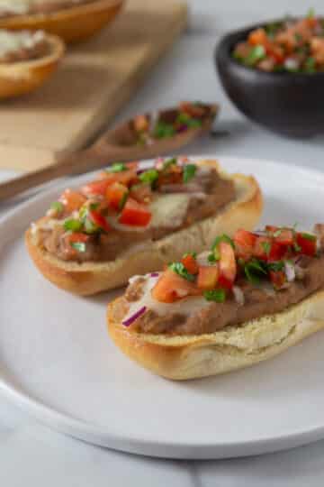 A photo of two molletes on a white plate with pico de gallo on top.