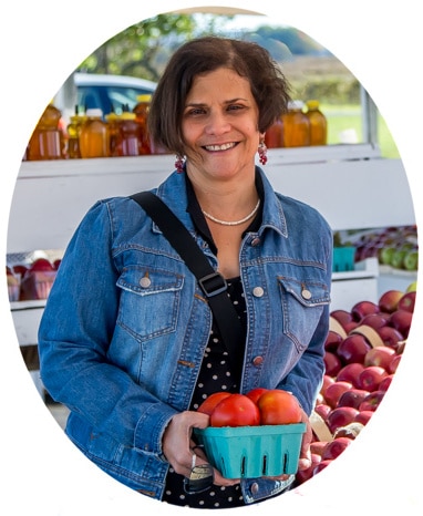 A photo of Analida at a farm stand with apples and tomatoes.