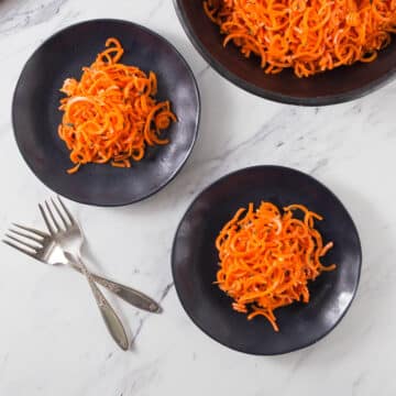 An overhead photo of Moroccan carrot salad on black plates with forks.