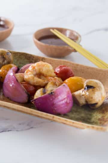 A plate with grilled shrimp, onions and mushrooms.