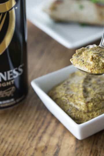 A spoon with homemade Guinness mustard with a dish and can of Guinness in the background.