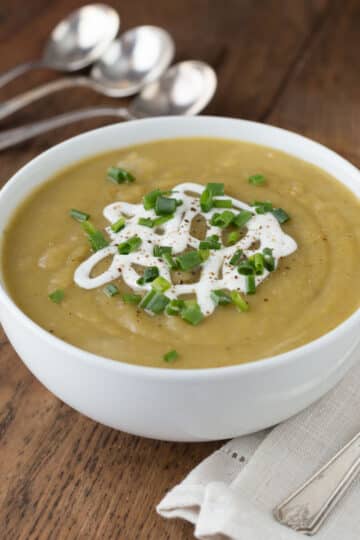 Irish potato leek soup in a white bowl with spoons in the background.