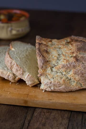 A loaf of Irish soda bread sliced on a wood cutting board.